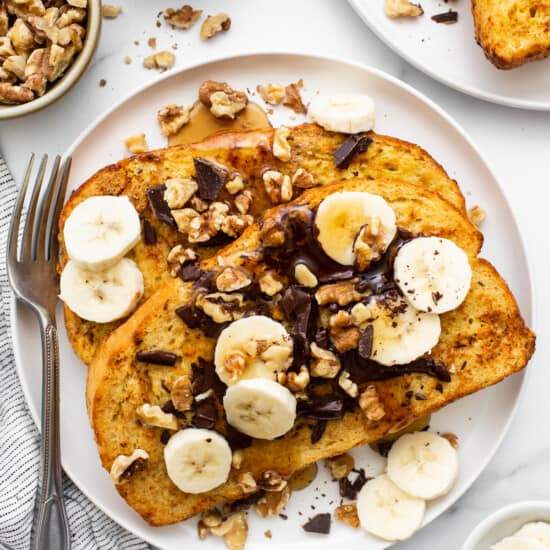 A plate of french toast with bananas, nuts and chocolate.