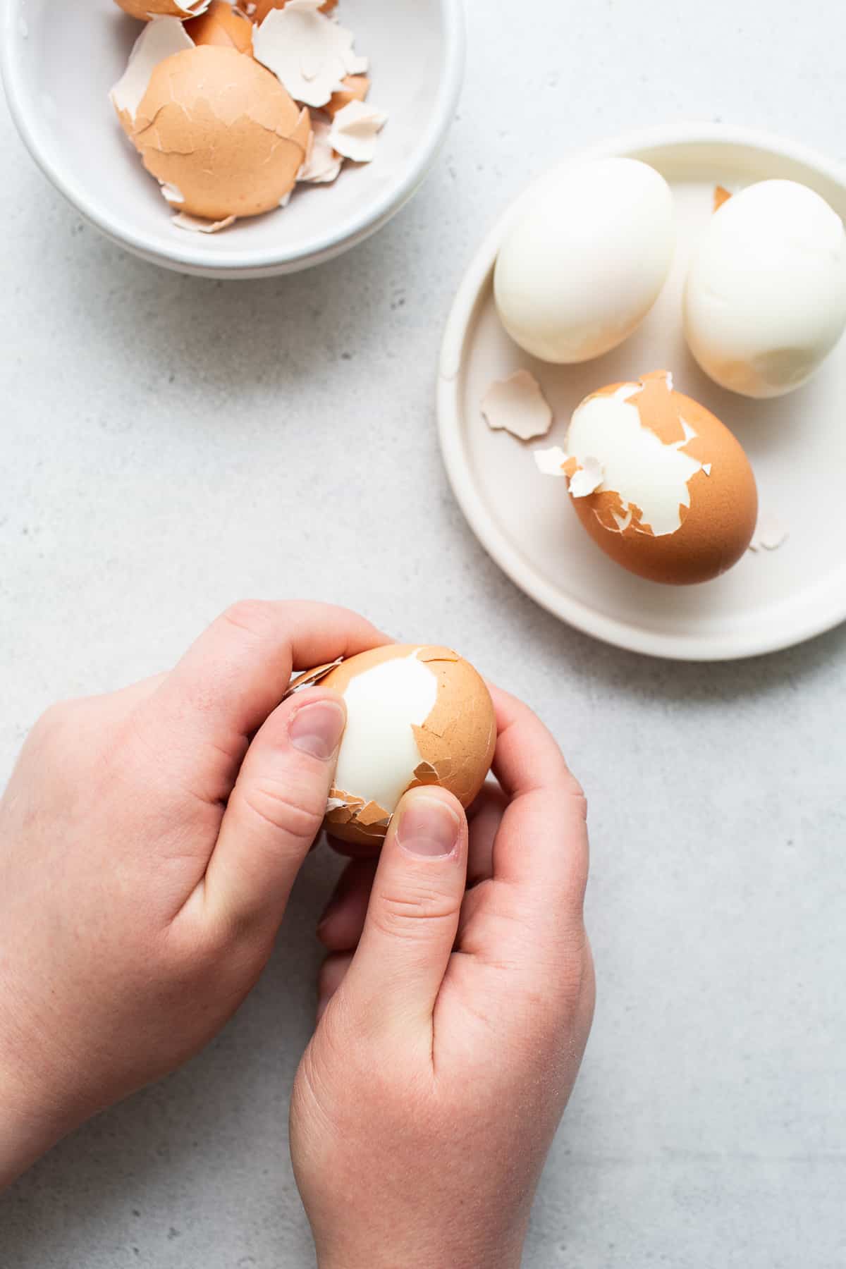 Hands peeling hard boiled eggs.
