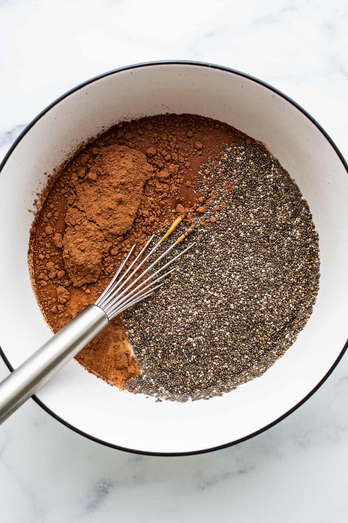 Chia seeds and cocoa powder in a bowl with a whisk.