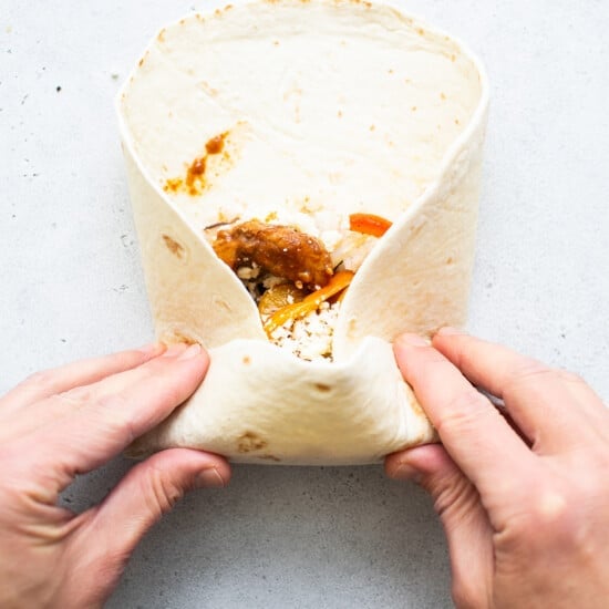 A person holding a burrito in their hands.