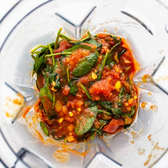 A blender filled with tomato sauce and spinach.