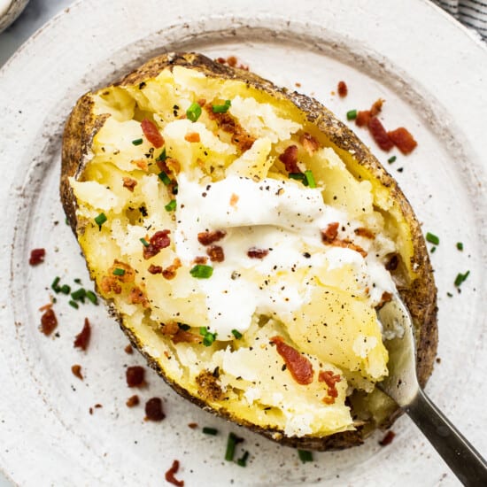 A baked potato topped with sour cream and bacon.