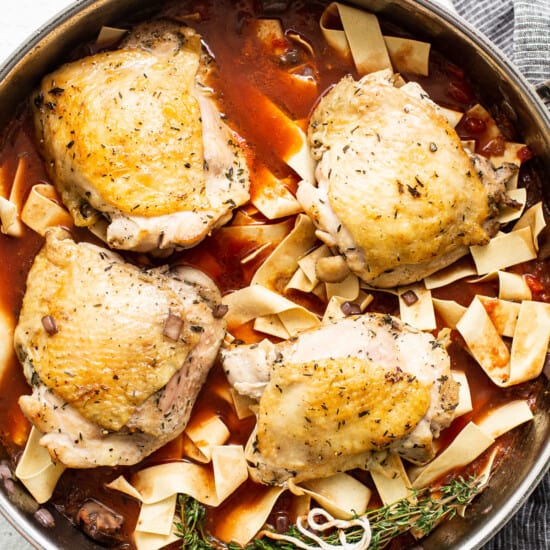 Chicken breasts in a pan with sauce and noodles.