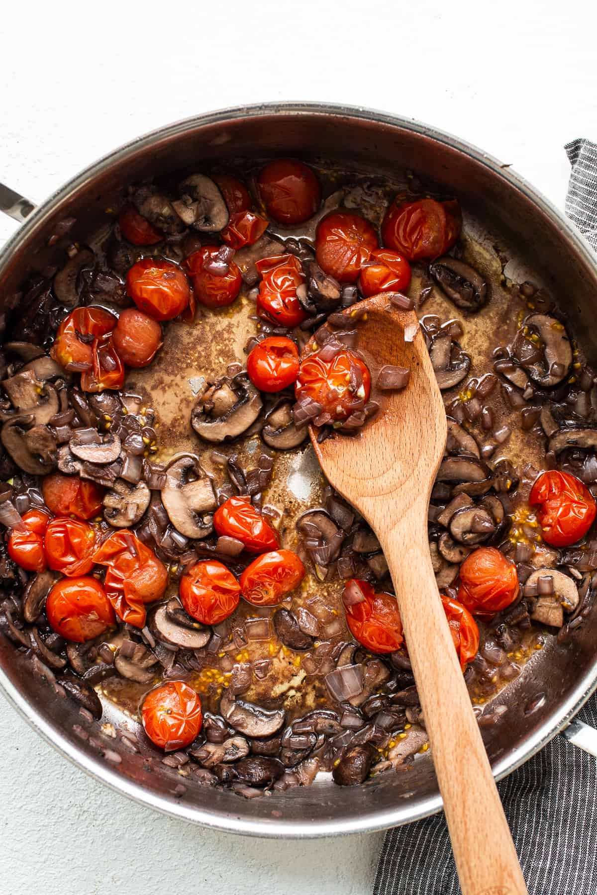 Mushrooms and tomatoes sautéing in a skillet.