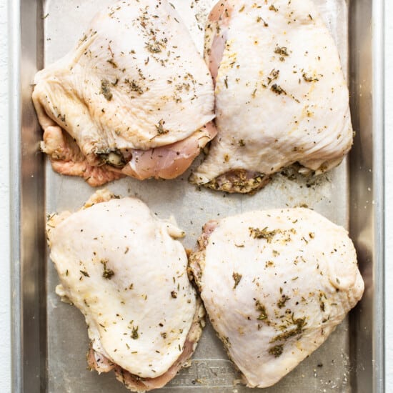 Chicken breasts on a baking sheet with herbs.