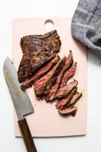 A piece of grilled steak on a pink cutting board.