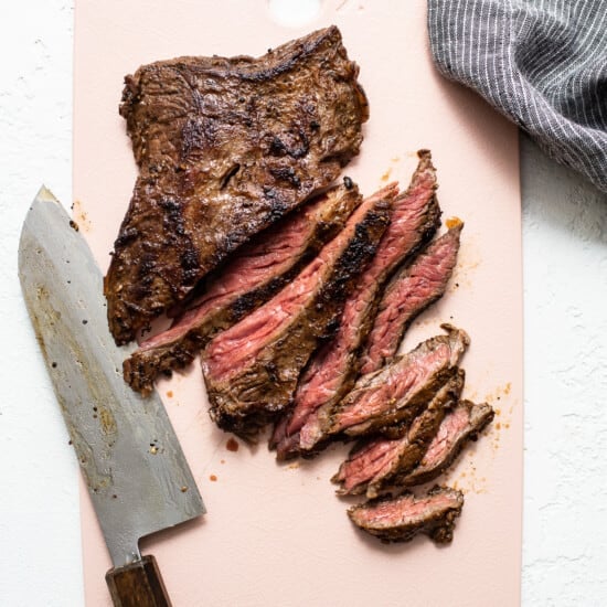 A piece of grilled steak on a pink cutting board.