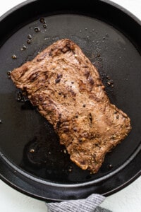 A piece of steak is being cooked in a pan.