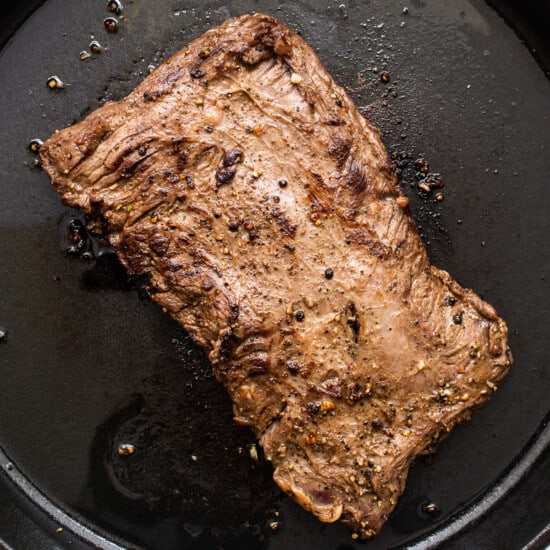 A piece of steak is being cooked in a pan.