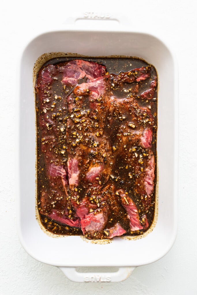 Skirt steak marinating in a baking dish. 