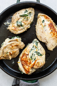 Chicken breasts with spinach and cheese in a skillet.