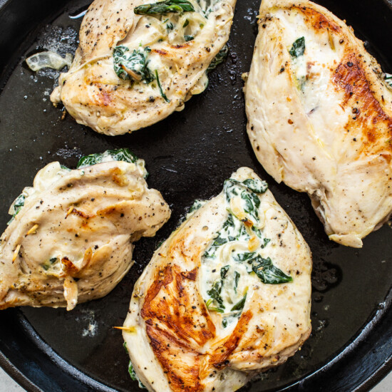 Chicken breasts with spinach and cheese in a skillet.