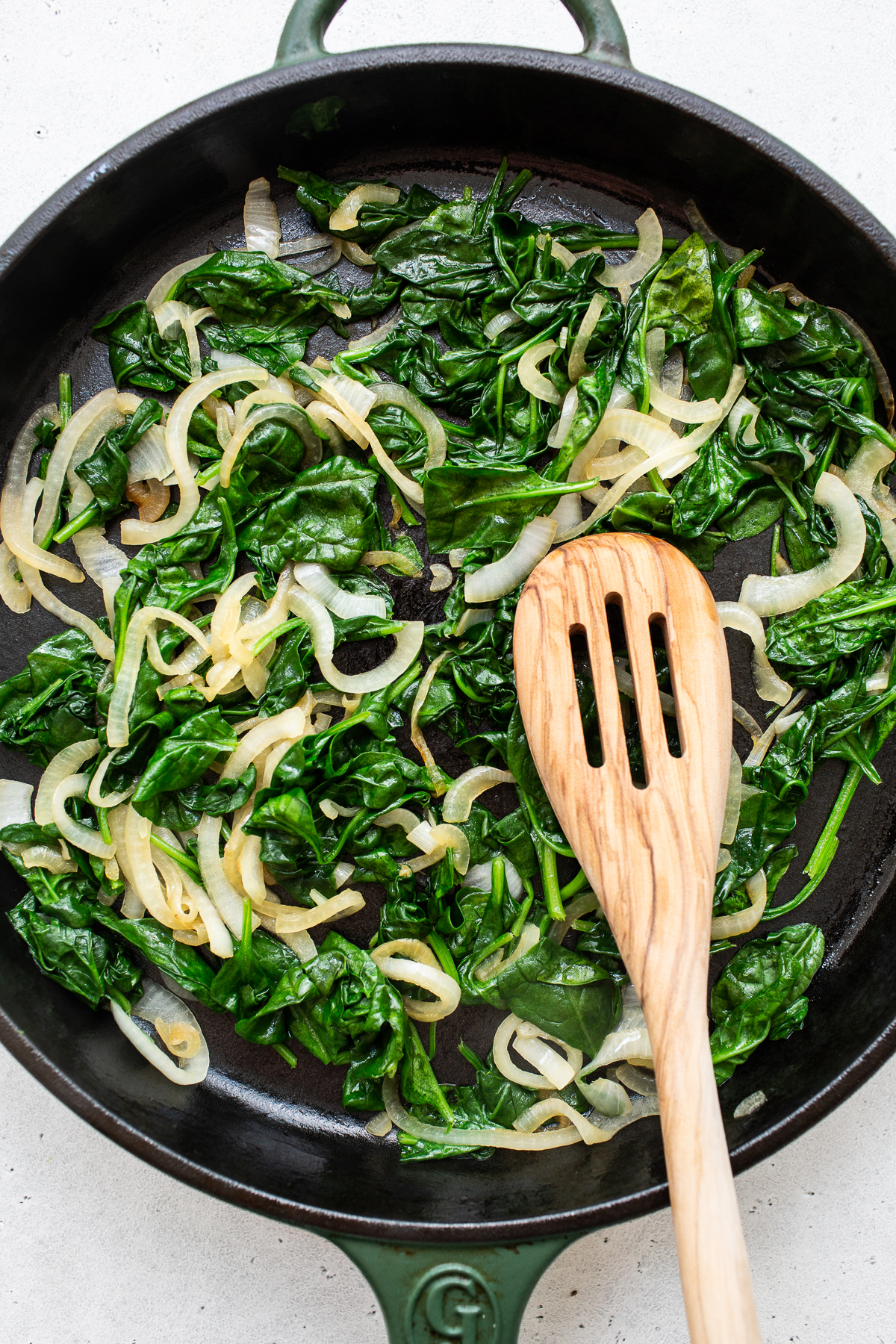Spinach and onions sauteing in a skillet.