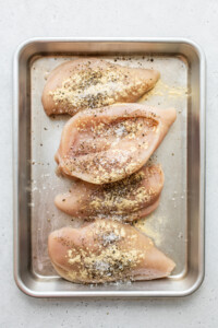 Chicken breasts on a baking sheet with seasonings.