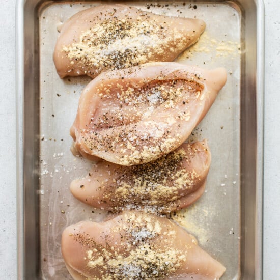Chicken breasts on a baking sheet with seasonings.
