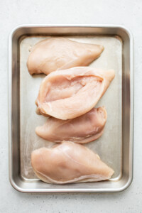 Four chicken breasts in a tray on a white background.