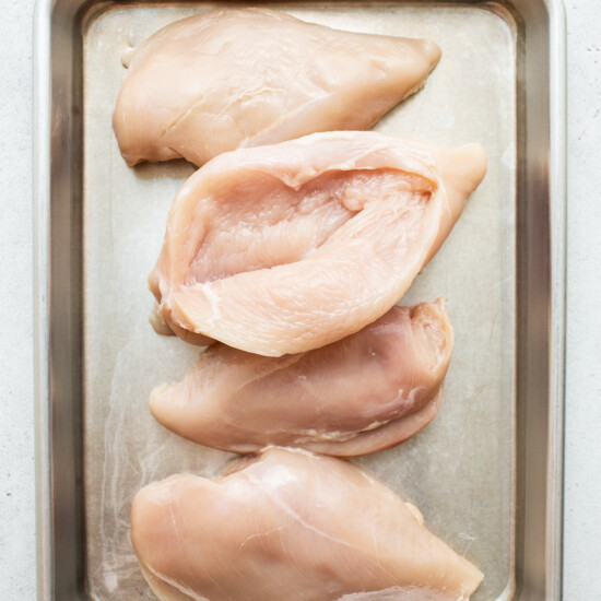 Four chicken breasts in a tray on a white background.
