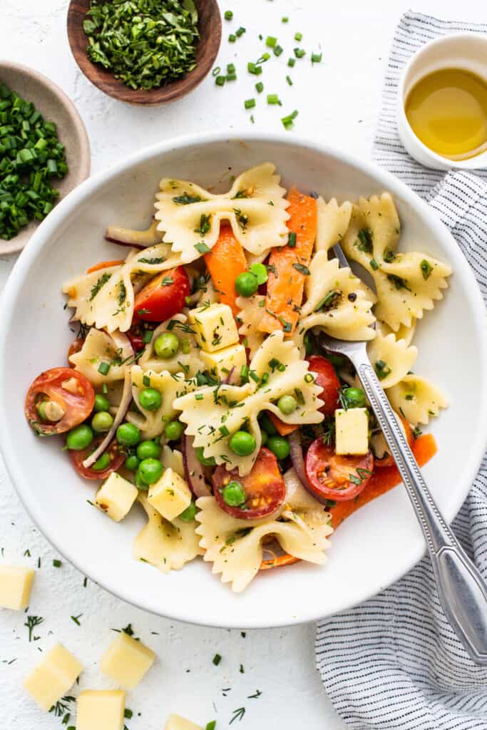 Bow tie pasta salad in a bowl topped with fresh herbs.