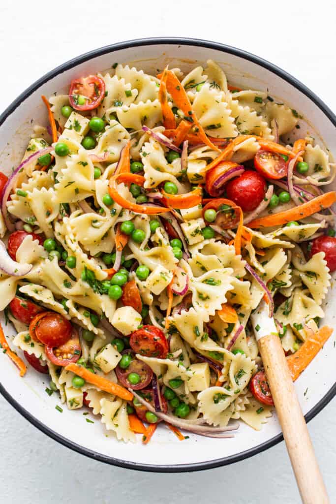 Bow tie pasta salad in a bowl with a spoon.
