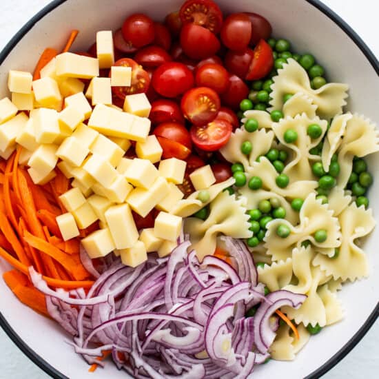 A bowl of pasta salad with carrots, peas and cheese.