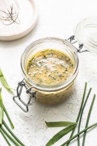 A jar with a green sauce and a whisk on a white background.