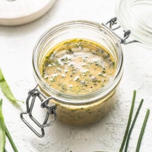 A jar with a green sauce and a whisk on a white background.