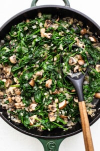 A skillet filled with spinach and mushrooms.