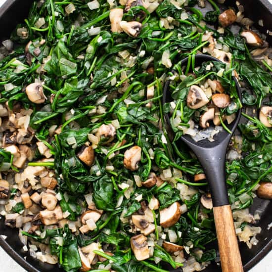 A skillet filled with spinach and mushrooms.