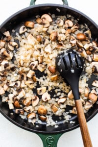 Mushrooms in a skillet with a wooden spoon.