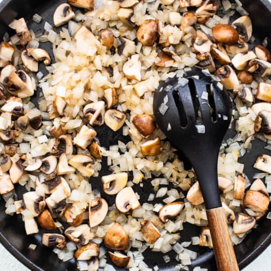 Mushrooms in a skillet with a wooden spoon.