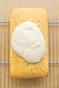 A loaf of bread with icing sitting on a cooling rack.