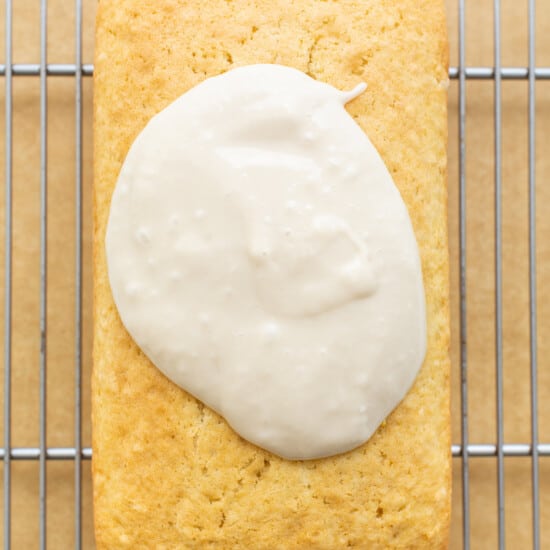 A loaf of bread with icing sitting on a cooling rack.