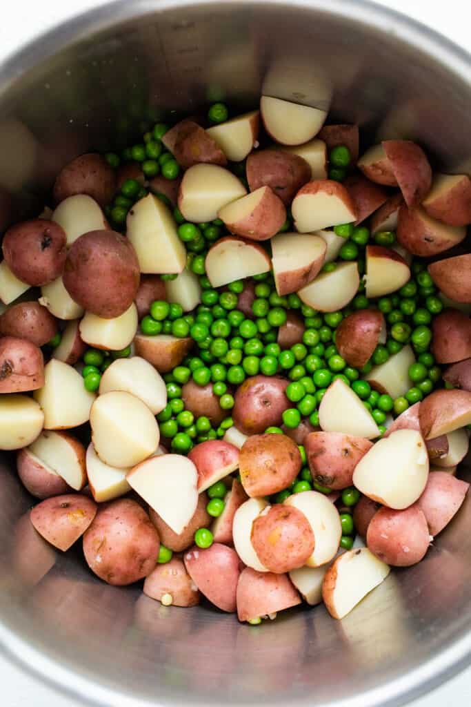 Red potatoes and english peas in a metal bowl.
