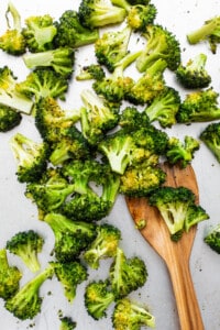 Chopped broccoli on a white plate with a wooden spoon.