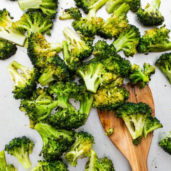 Chopped broccoli on a white plate with a wooden spoon.