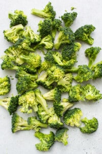 A pile of chopped broccoli on a white surface.