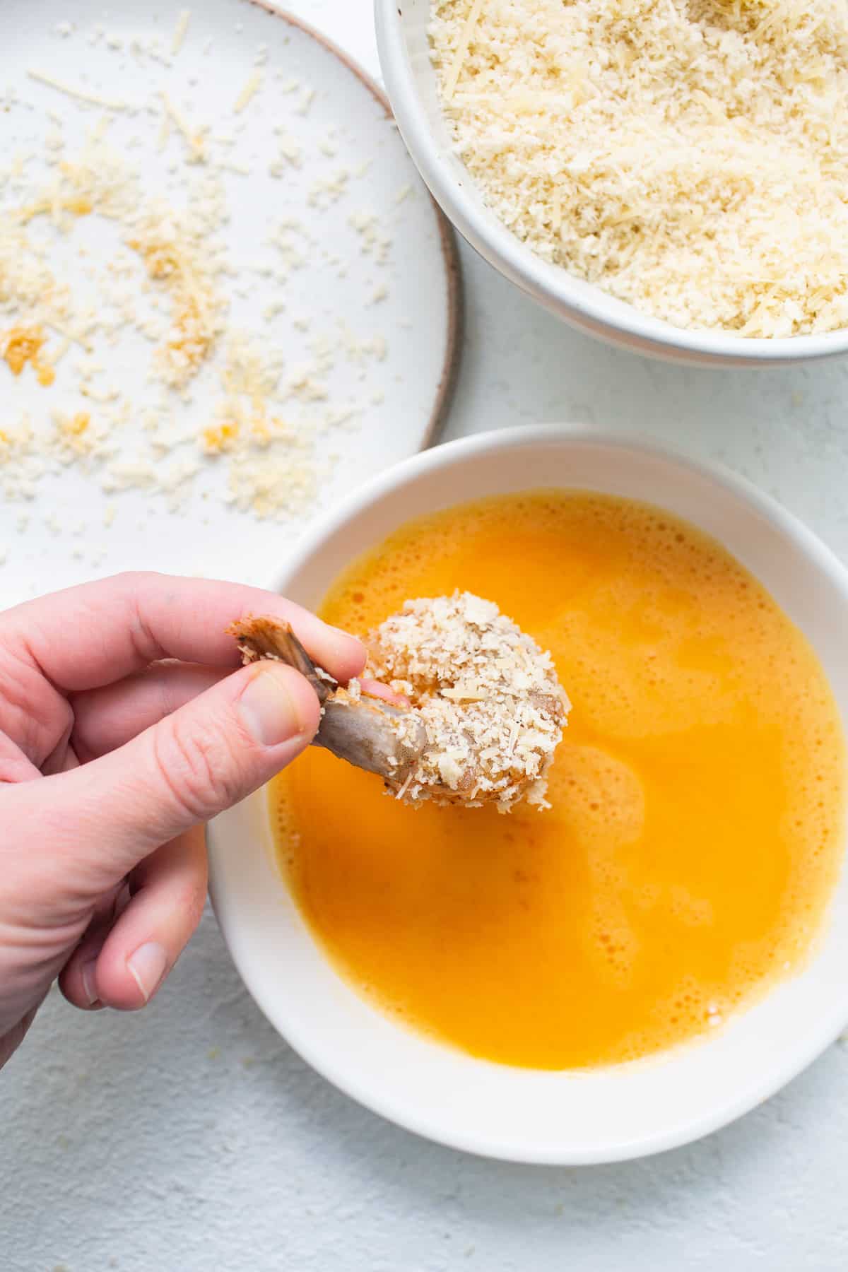 Panko coated shrimp being dipped into an egg wash.