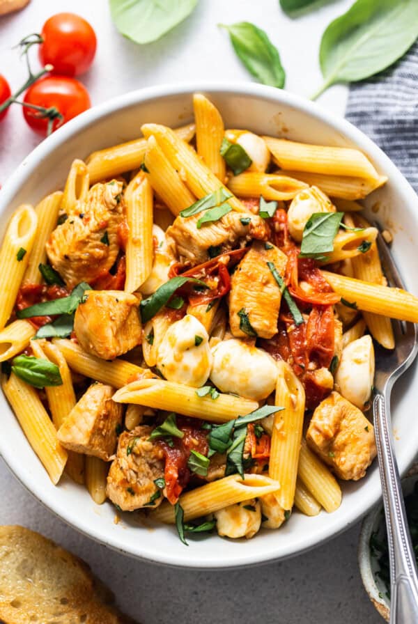 caprese chicken pasta in bowl with fork.