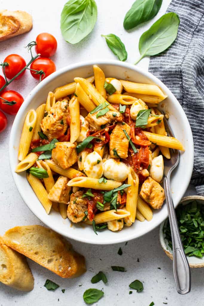 caprese chicken pasta in bowl with crostini on the side.