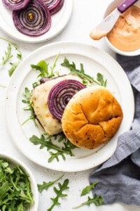 A plate of burgers with red onions and arugula.