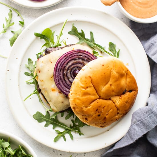 A plate of burgers with red onions and arugula.