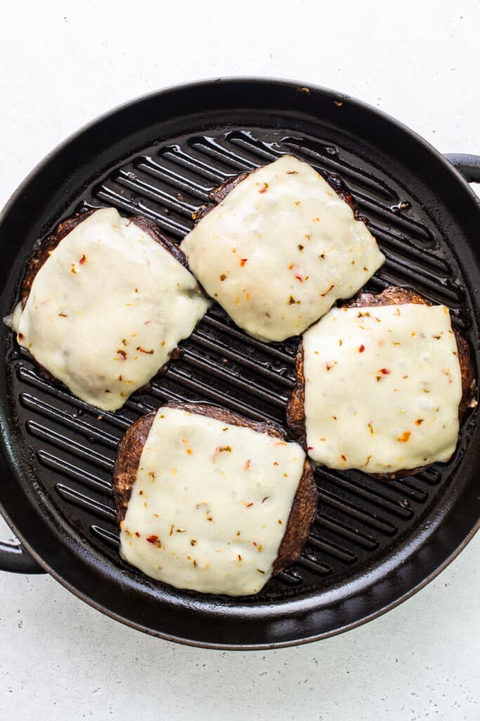 Portobello mushroom burgers topped with cheese on a grill plan.