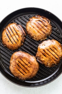 Four grilled burgers in a pan on a white background.