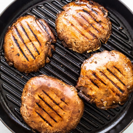 Four grilled burgers in a pan on a white background.