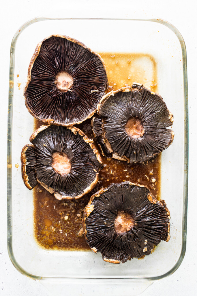 Portobello mushrooms marinating in a baking dish.