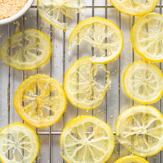 Sliced lemons on a cooling rack next to a bowl of sugar.