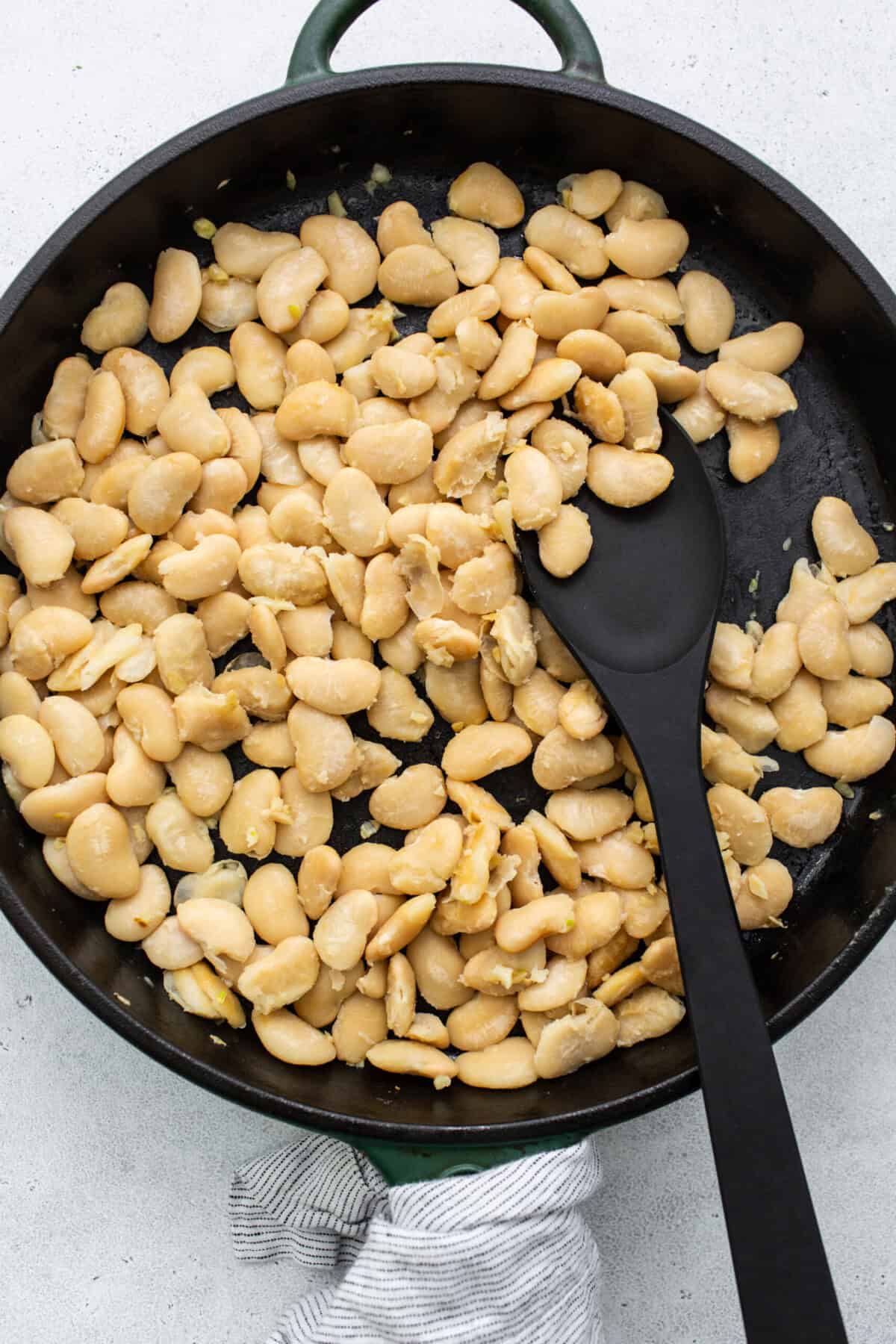 White beans in a frying pan with a black spatula.