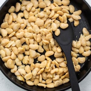 White beans in a frying pan with a black spatula.