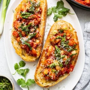 Two slices of bread with tomato sauce and herbs on a plate.