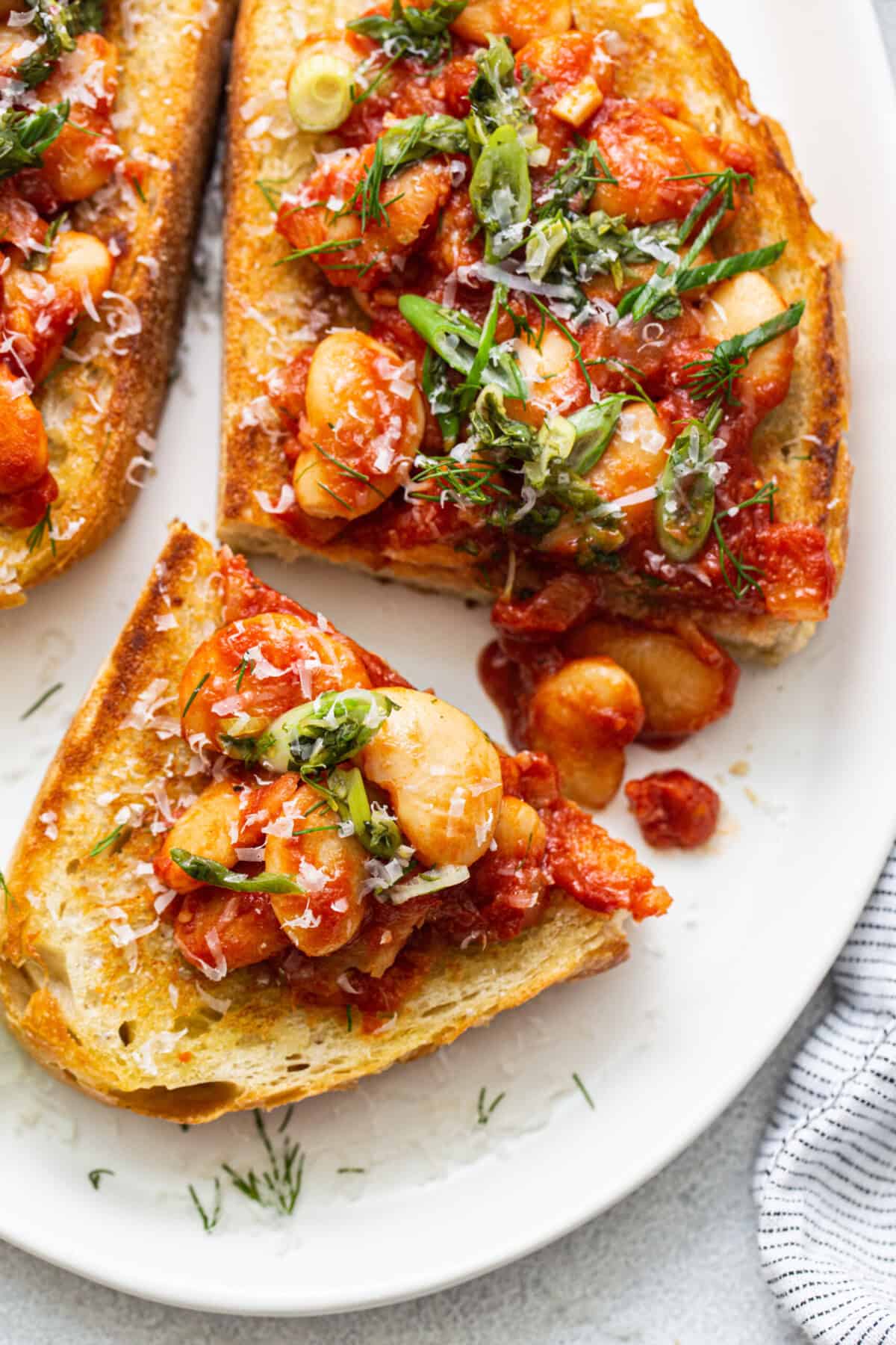 Two slices of toast with tomatoes and herbs on a plate.